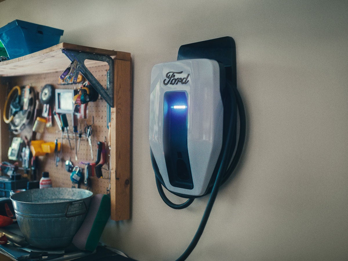 A Ford Charge Station Pro mounted on a garage wall with tools hanging next to it.